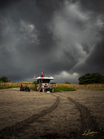 Lifeguard tower with double red flags on an empty beach, illuminated by golden light as a severe storm with dark clouds approaches in the background.