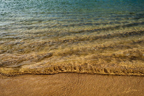 Golden light reflecting on shallow waves and sand in Juno Beach.