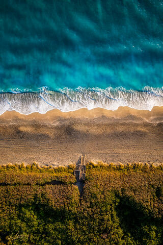 Aerial top-down photograph of a wooden boardwalk and staircase leading to turquoise ocean waters on Juno Beach in Palm Beach County, Florida.