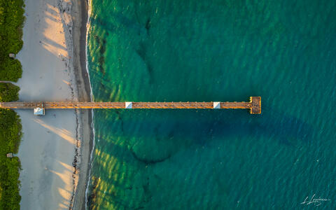 Aerial overhead photograph of Juno Beach Pier at sunset with long shadows cast over emerald water in Jupiter / Juno Beach, Palm Beach County, Florida.