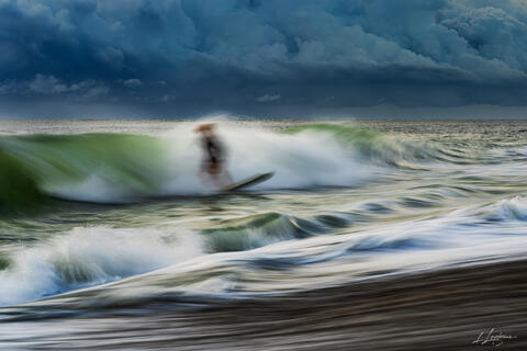 Long exposure photograph of a surfer riding a wave under storm clouds at Jupiter, Florida. 
Fine art seascape by Lawrence Leyderman.