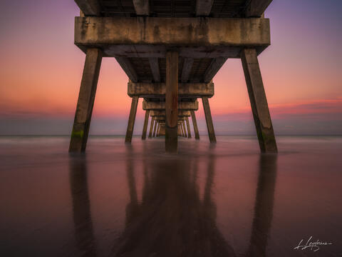 Under the Juno Beach Pier at sunrise with calm reflections and symmetry.