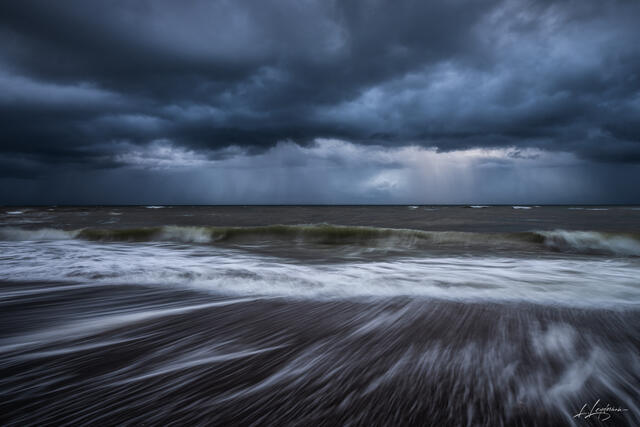 Long exposure photograph of waves receding under dark storm clouds along the Jupiter coastline in Florida. Fine art seascape by Lawrence Leyderman.
