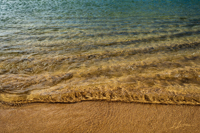 Golden light reflecting on shallow waves and sand in Juno Beach.
