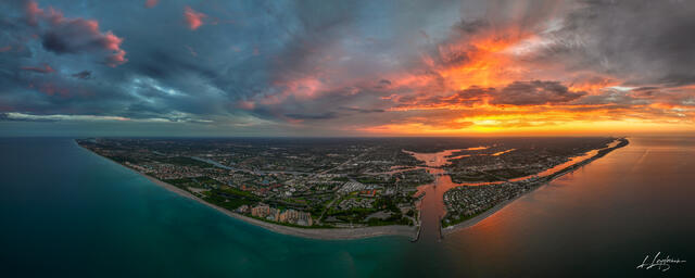 Aerial panoramic photograph of a vibrant fiery sunset over Jupiter Inlet and Juno Beach Pier in Palm Beach County, Florida, with dramatic orange and red clouds 