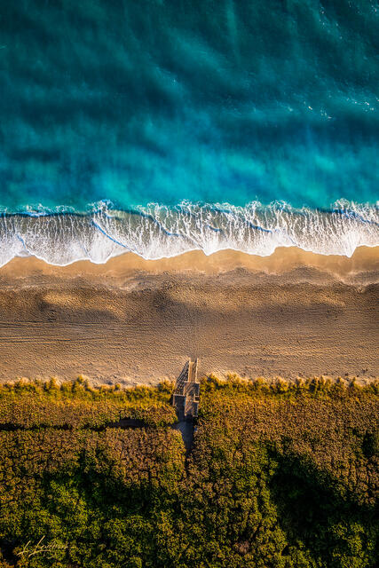 Aerial top-down photograph of a wooden boardwalk and staircase leading to turquoise ocean waters on Juno Beach in Palm Beach County, Florida.