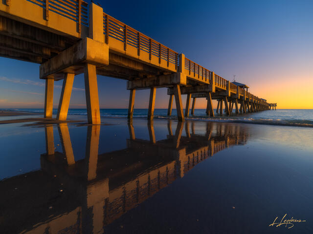 Sunrise reflections on wet sand near Juno Beach Pier.