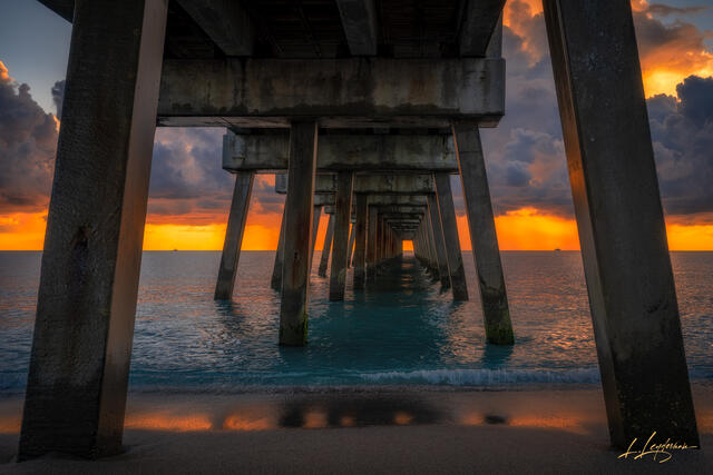 Wide view of Juno Beach Pier at a vivid orange sunrise.