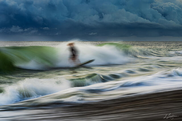 Long exposure photograph of a surfer riding a wave under storm clouds at Jupiter, Florida. 
Fine art seascape by Lawrence Leyderman.