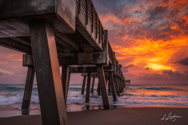 Juno Beach Pier beneath a vivid red and orange sunrise sky.