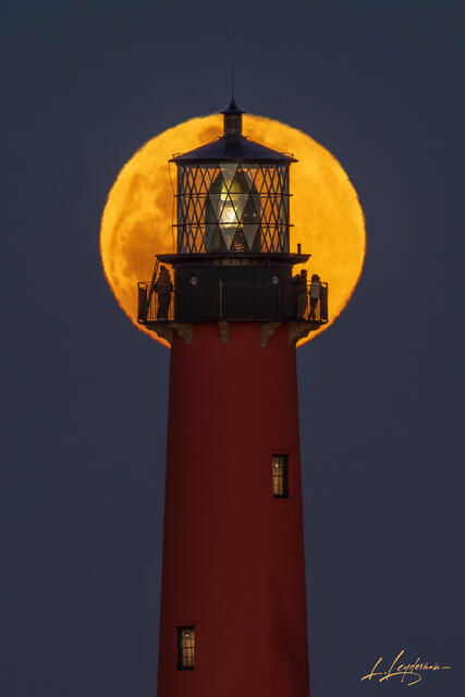 Jupiter Inlet Lighthouse silhouetted against a large golden Snow Moon at night.