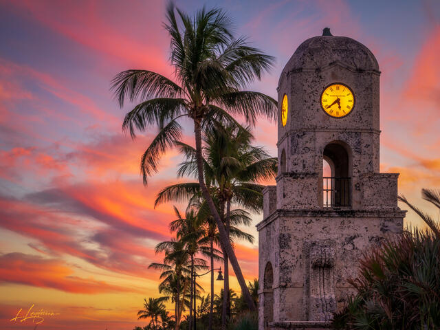 Historic Worth Avenue clock tower glowing at sunset during blue hour, framed by palm trees beneath a colorful evening sky in Palm Beach, Florida.