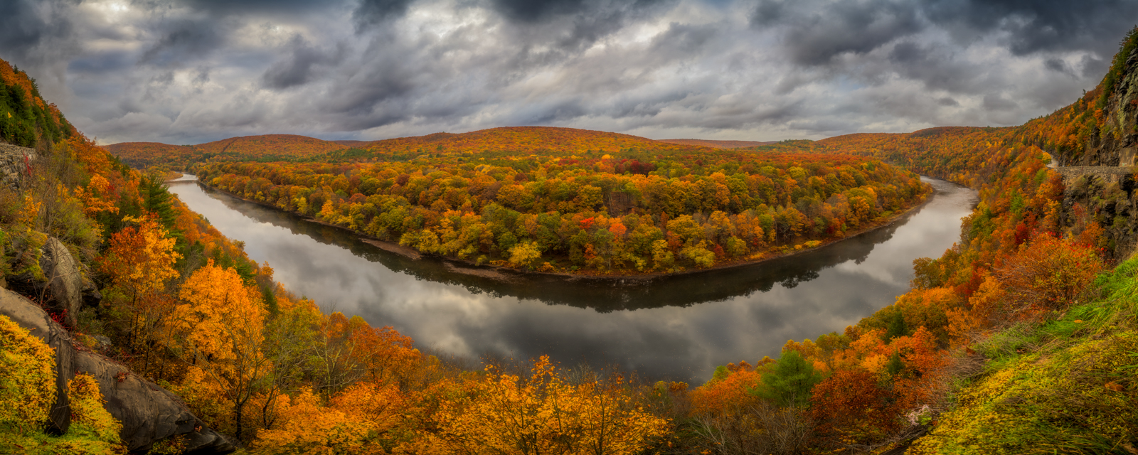 In this serene snapshot of a New England fall, the river bends in a graceful arc, cradled by a kaleidoscope of trees in their...