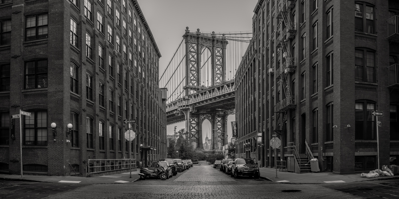 The grandeur of the Manhattan Bridge rises majestically at the end of this urban canyon, flanked by the timeless facades of Dumbo...